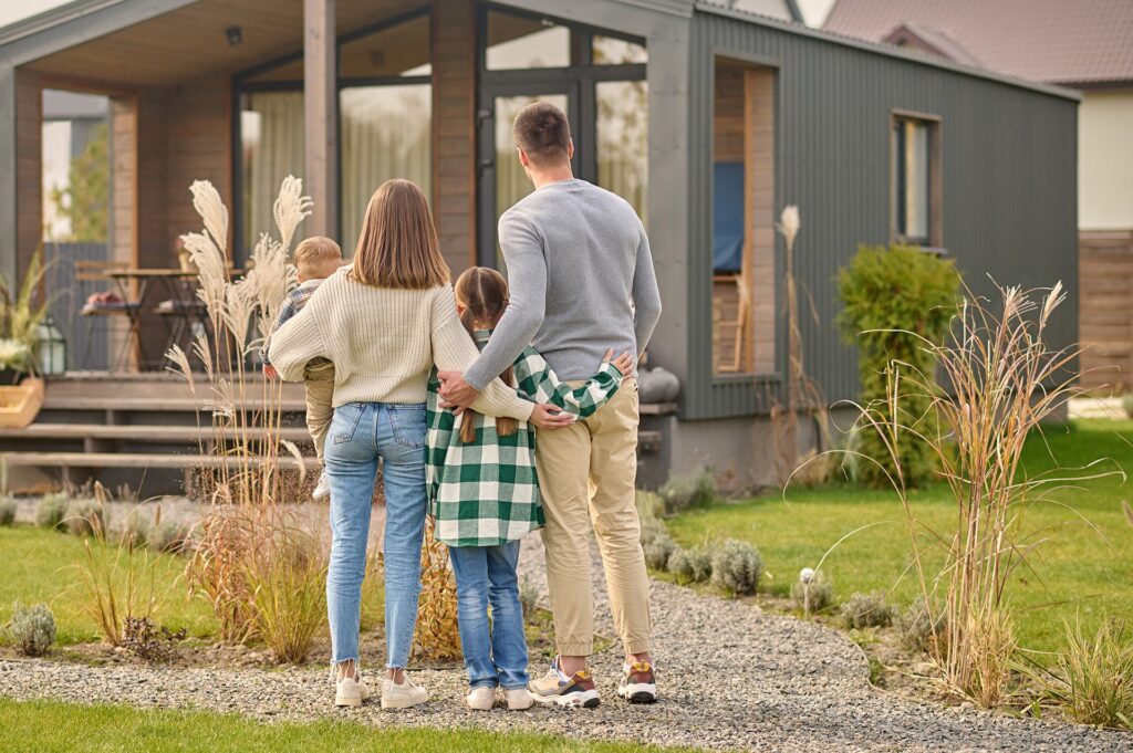 Junge Familie mit zwei Kindern steht vor fertig gebautem modularem Container Haus mit Holzausbau