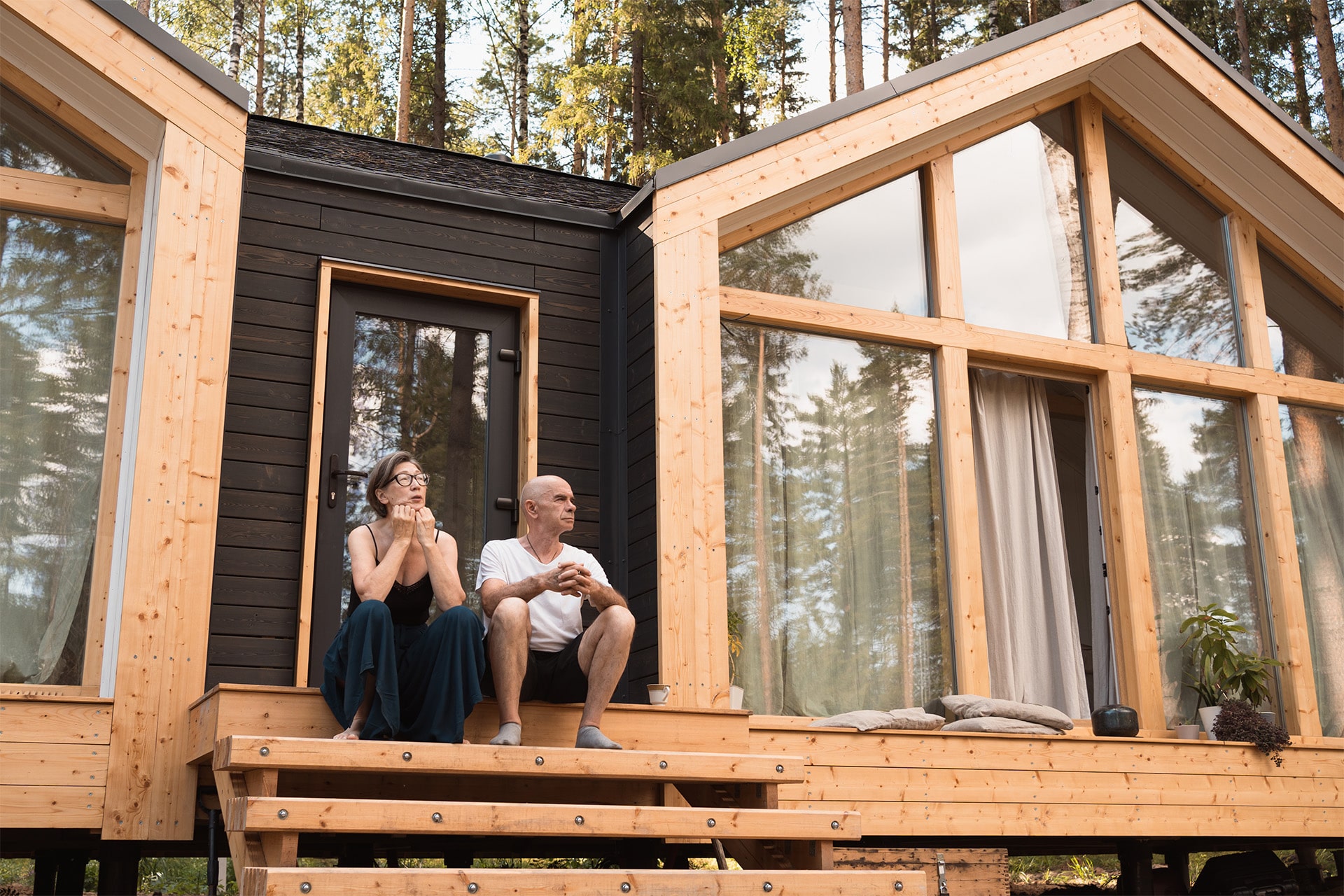 Älteres Pärchen sitzt vor neuem Tiny Home aus Holz in modularer Bauweise.
